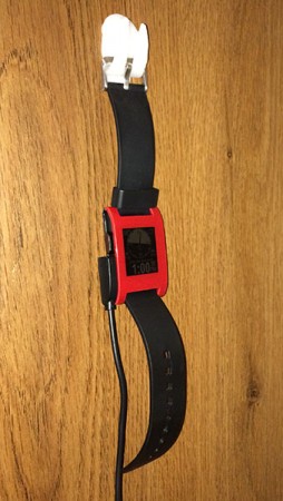 Pebble Watch hanging from InstaMorph holder with charging cable on the side.